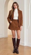 Front full view of woman wearing brown corduroy blazer and belted mini skirt set with knee-high boots