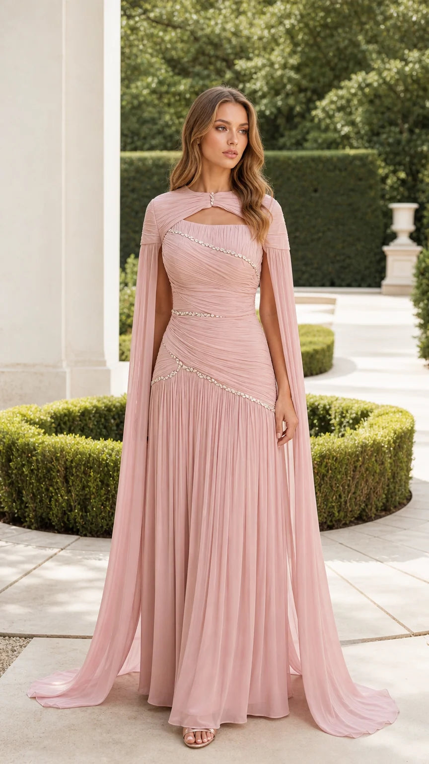 Front view of woman wearing dusty pink ruched evening gown with dramatic cape sleeves and crystal waist detail