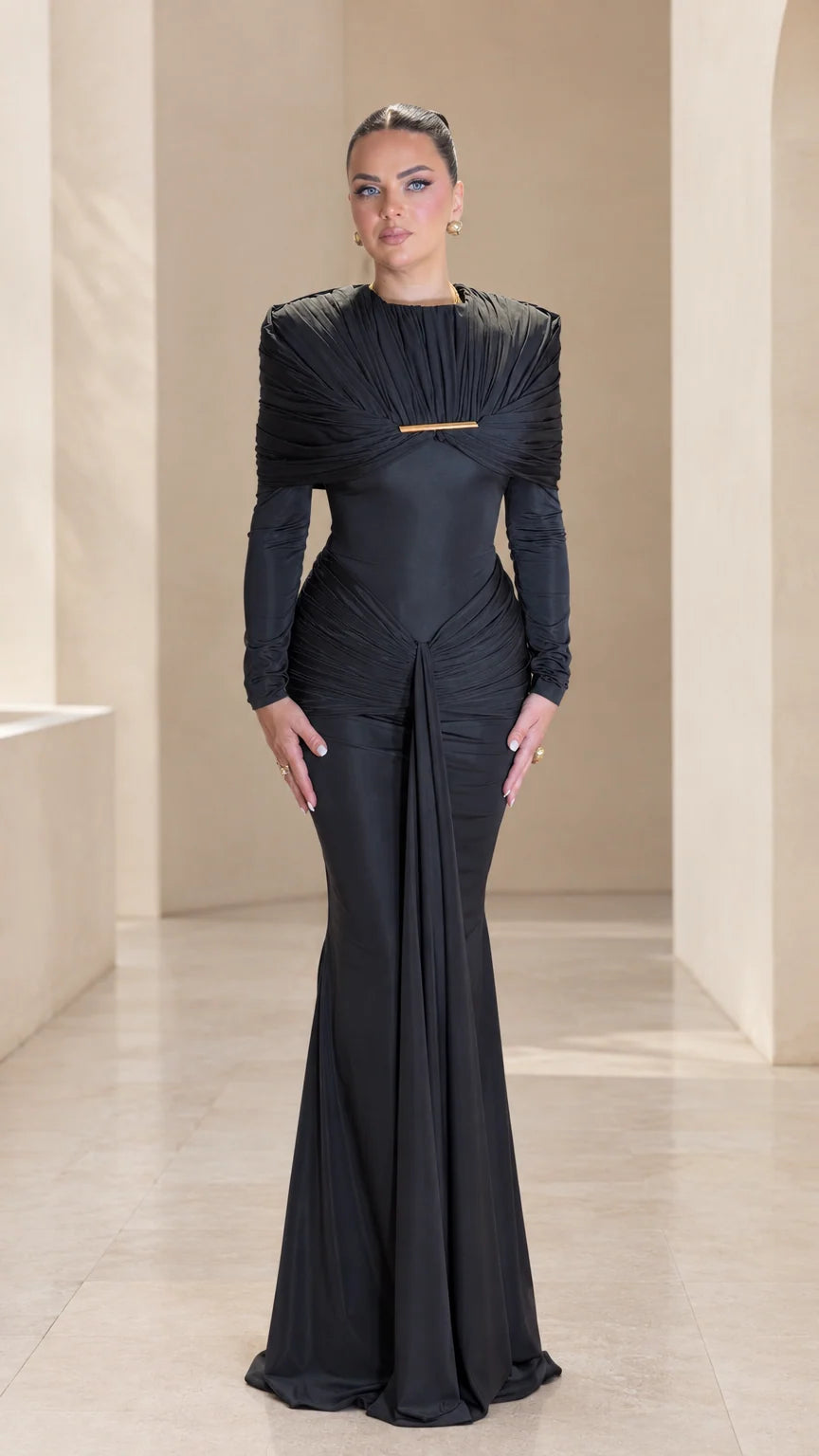 Front full view of black pleated cape long sleeve maxi evening gown with gold bar accent