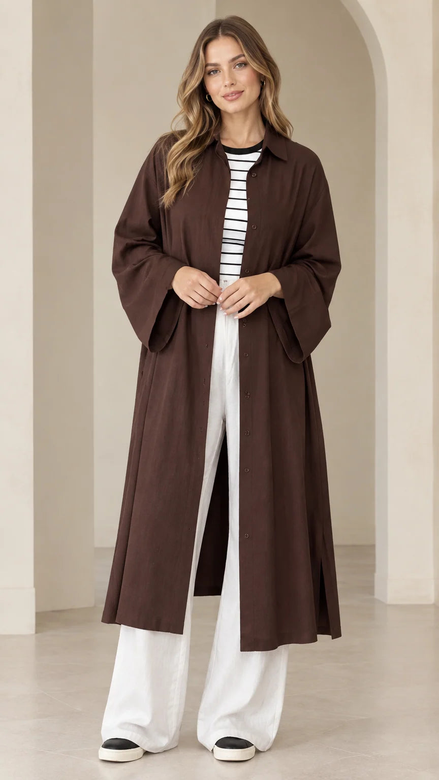 Front view of model wearing dark brown longline duster shirt dress with white wide-leg trousers