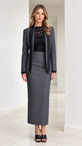 Front full-length view of woman wearing charcoal grey tailored blazer and maxi skirt suit with black lapel trim