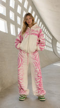 Front view of model wearing cream and pink abstract zebra print zip hoodie and sweatpants set