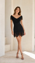 Front view of model wearing black off-the-shoulder fringe trim bodycon mini dress with black heels