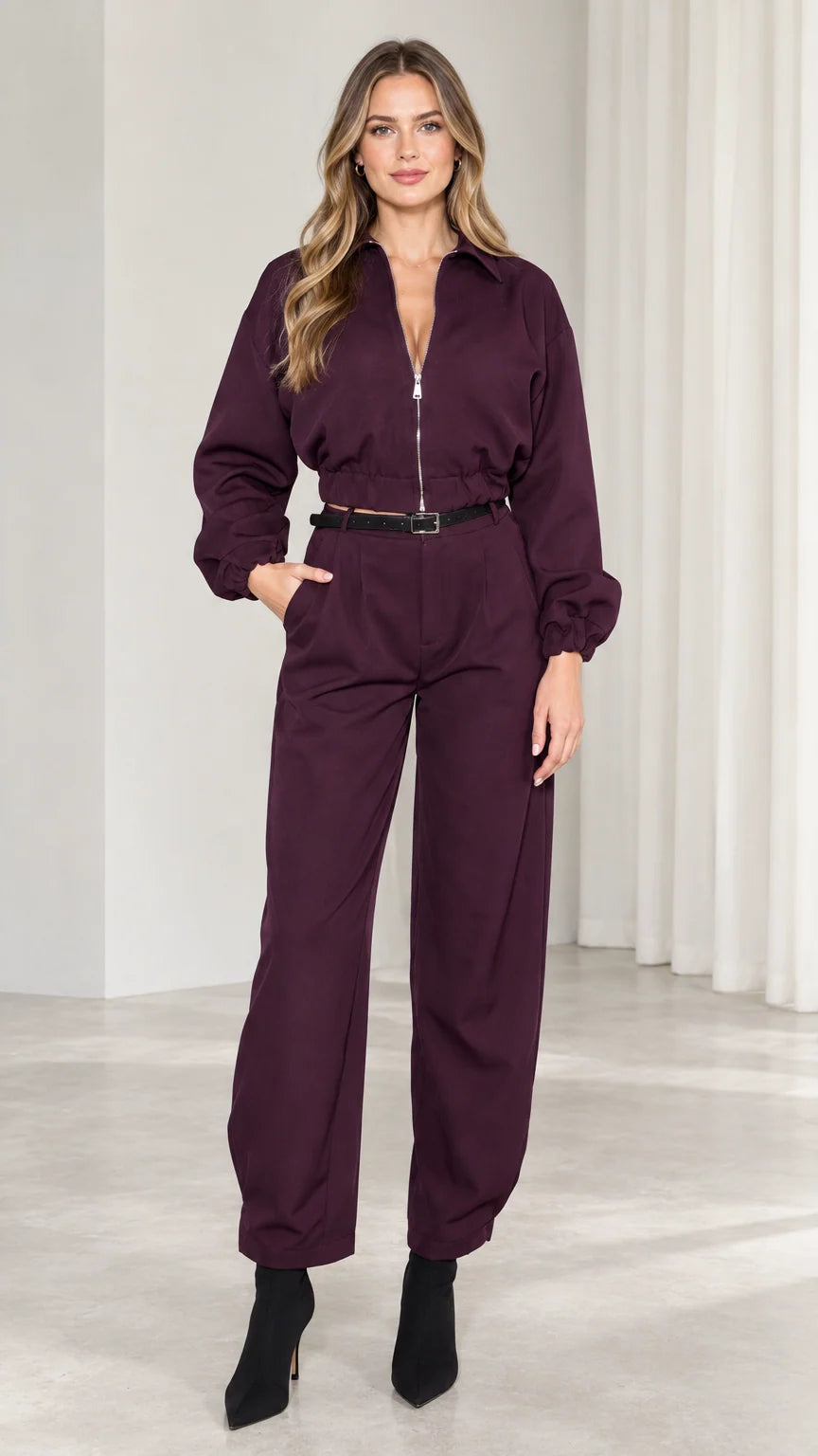 Front view of model wearing burgundy long sleeve zip front utility jumpsuit with black belt