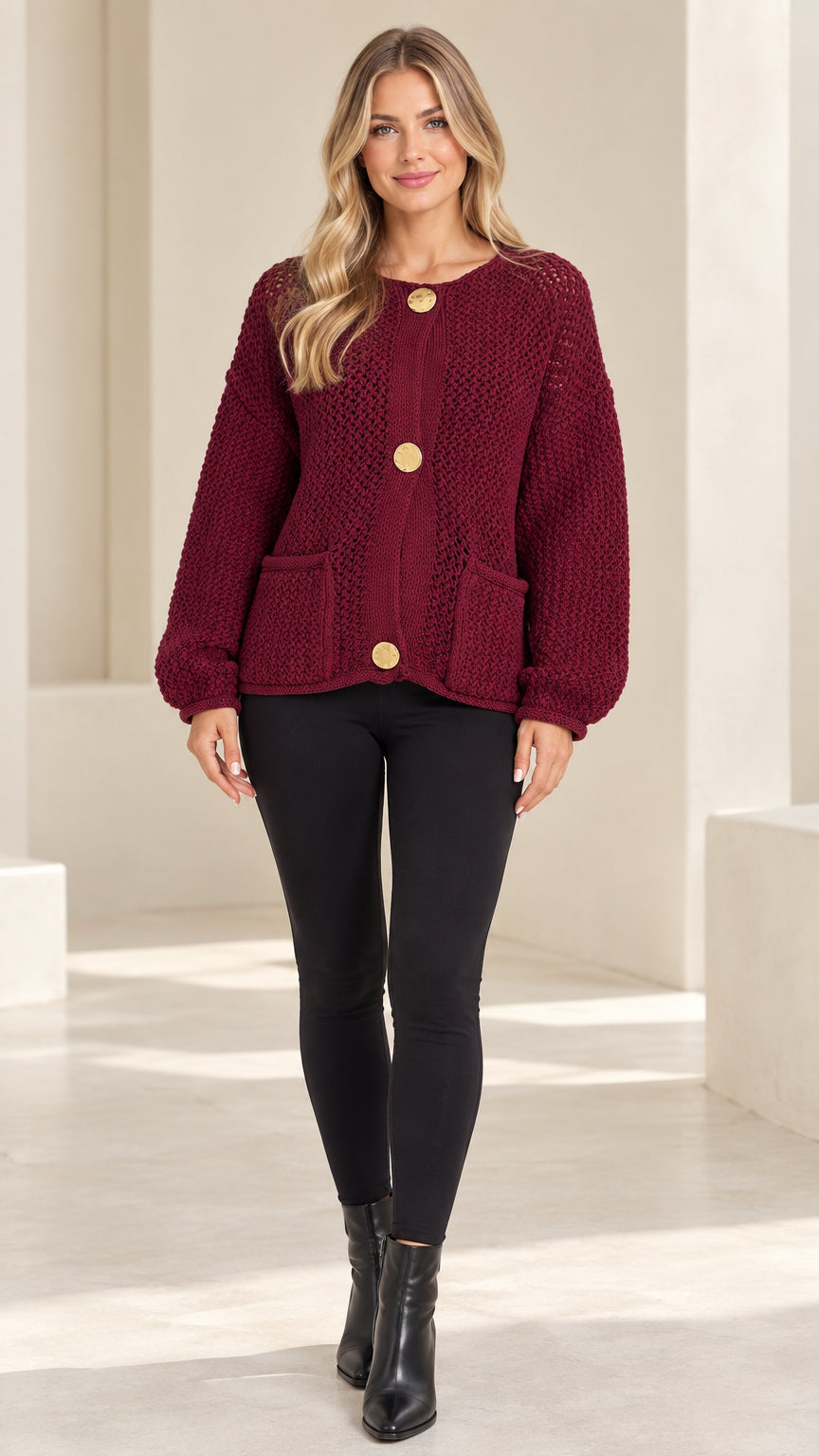 Front full-length view of model wearing burgundy textured chunky knit cardigan with gold buttons and black leggings