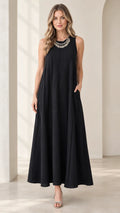 Front full-length view of woman wearing black sleeveless panel swing maxi dress with statement necklace