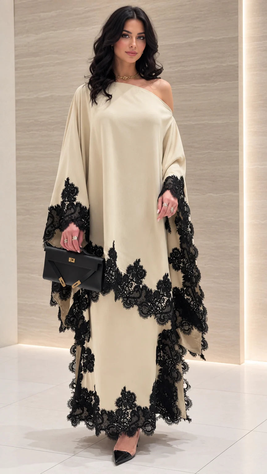 Front view of woman wearing cream one-shoulder draped maxi dress with black lace trim
