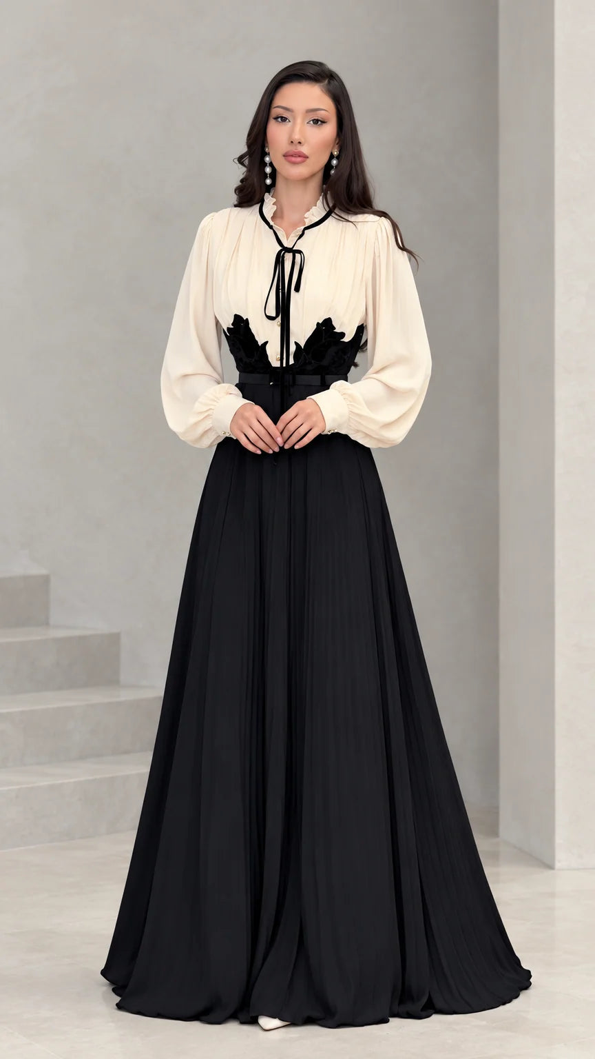 Full front view of model wearing cream and black pleated maxi dress with waist applique