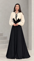 Full front view of model wearing cream and black pleated maxi dress with waist applique