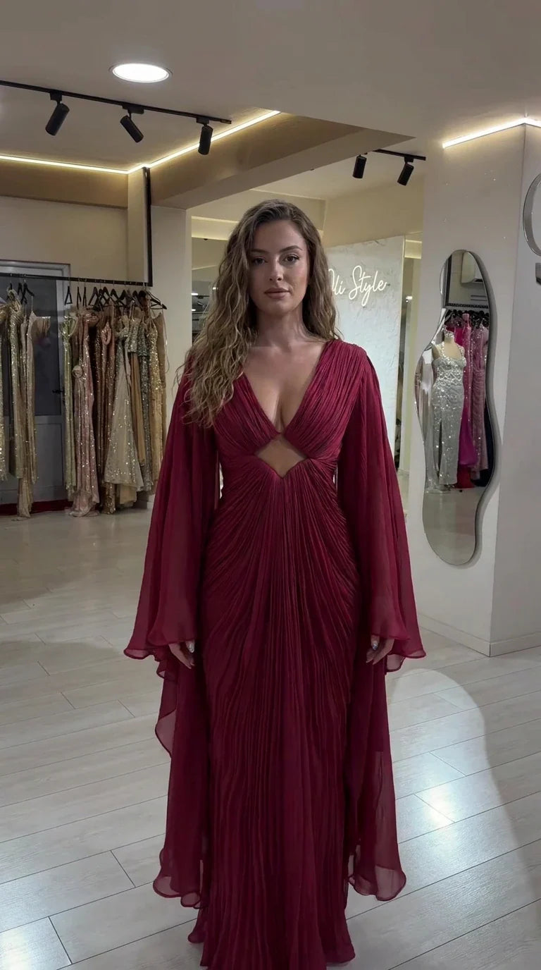 Front view of model wearing burgundy pleated maxi evening gown with cape sleeves and front cutout
