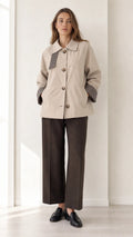 Front view of women's beige short trench jacket with houndstooth trim and dark trousers