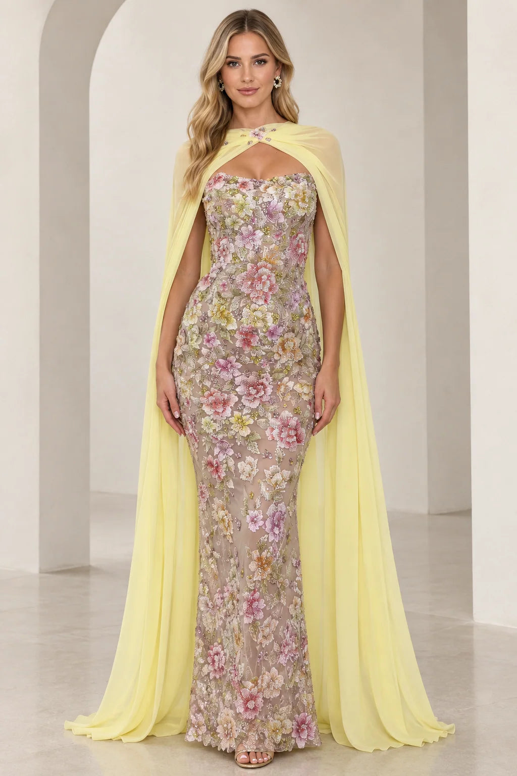 Front view of model wearing yellow floral embroidered strapless evening gown with matching sheer cape