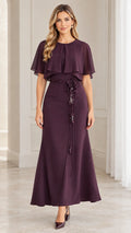Front full-length view of woman wearing plum chiffon capelet maxi dress with floral waist tie