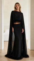 Front view of black two-piece evening gown with feather-trimmed cape top and maxi skirt