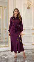 Woman wearing a burgundy satin-look embroidered maxi shirt dress with tie waist and front slit