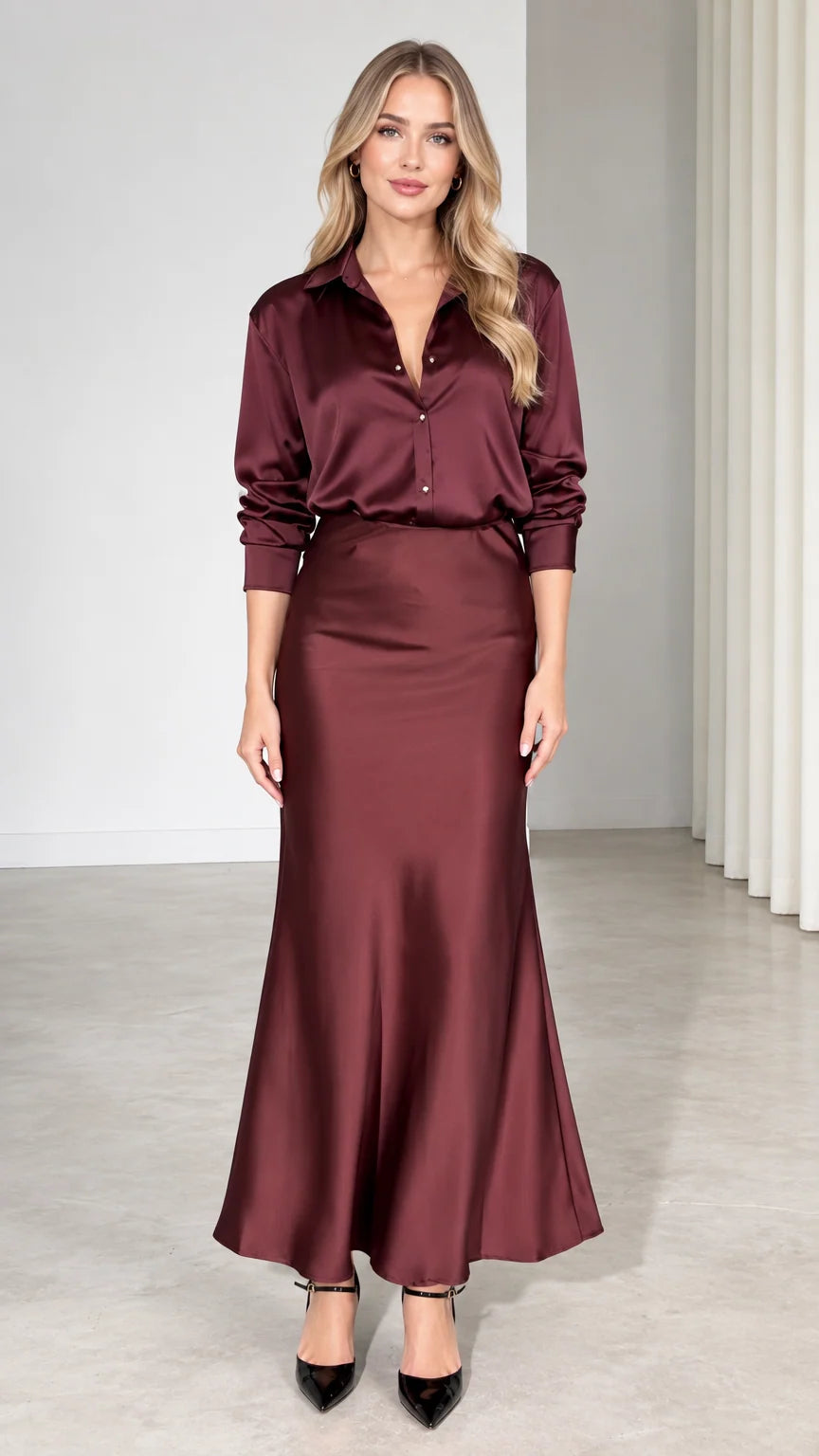Front view of model wearing burgundy satin button-down shirt and matching maxi skirt set