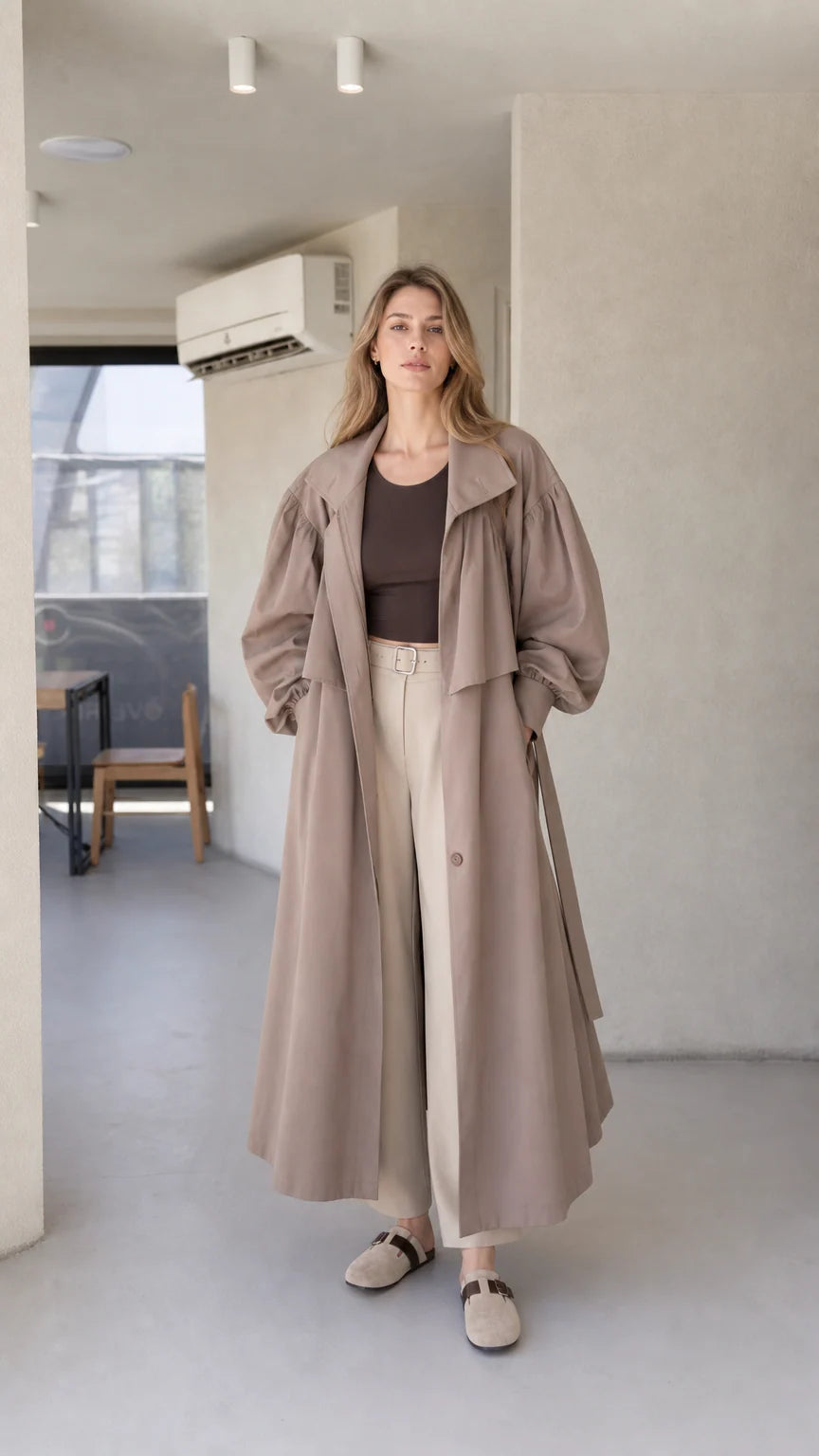 Front view of model wearing a taupe brown oversized maxi trench coat with balloon sleeves and tie belt