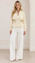 Front full-length view of woman wearing cream peplum trench jacket with white wide-leg pants