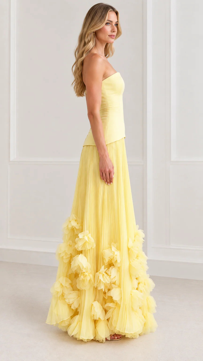 Side profile of model in yellow pleated strapless evening gown with floral details