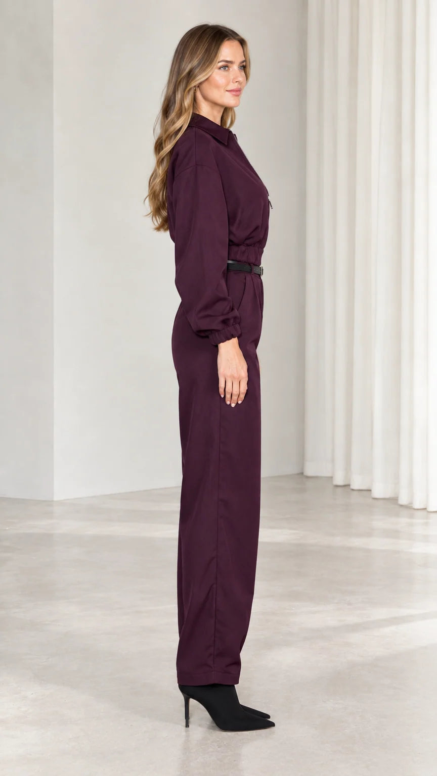 Side profile view of burgundy belted utility jumpsuit with long sleeves