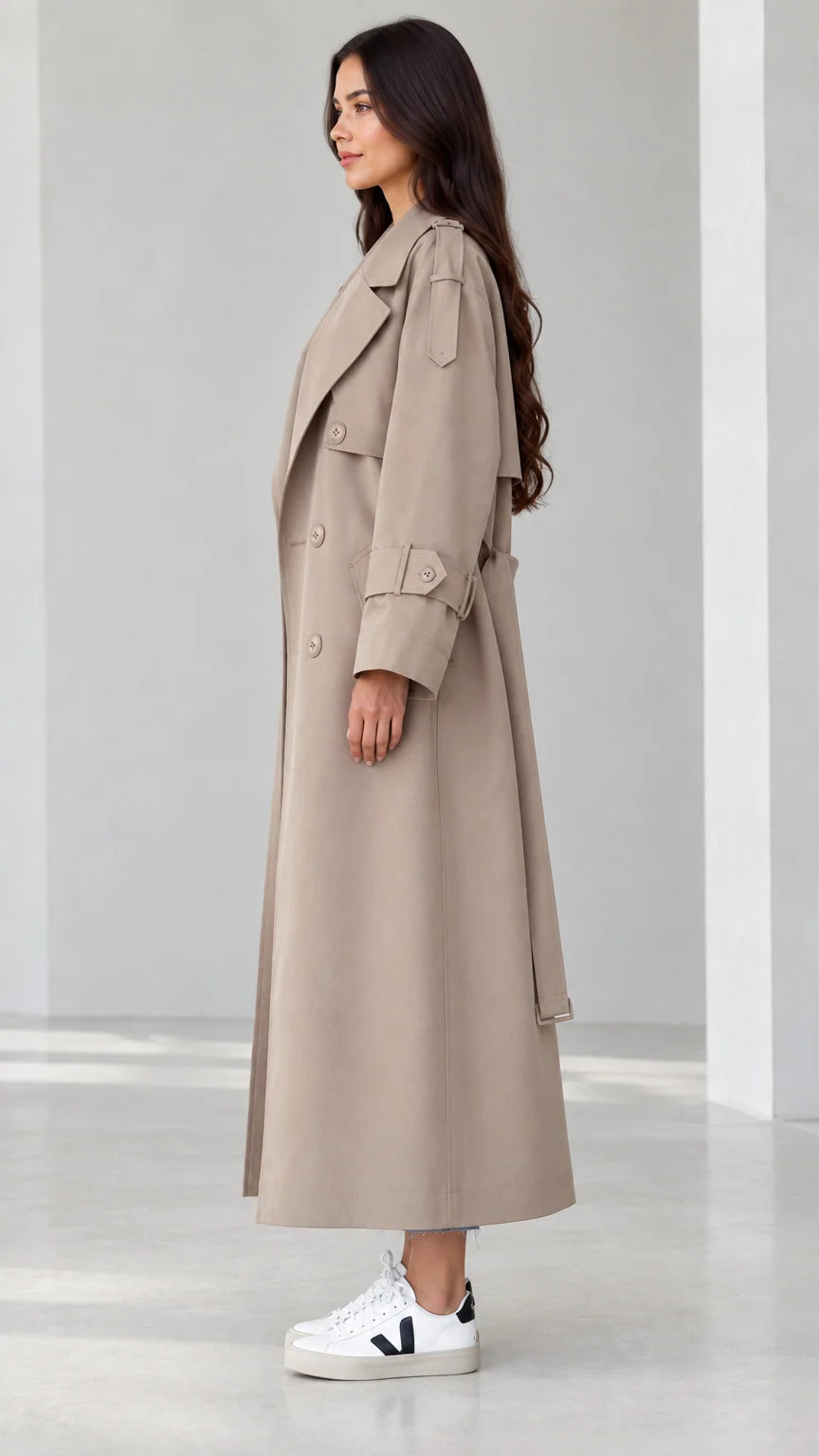 Side profile view of women's beige maxi trench coat showing sleeve straps and fluid drape