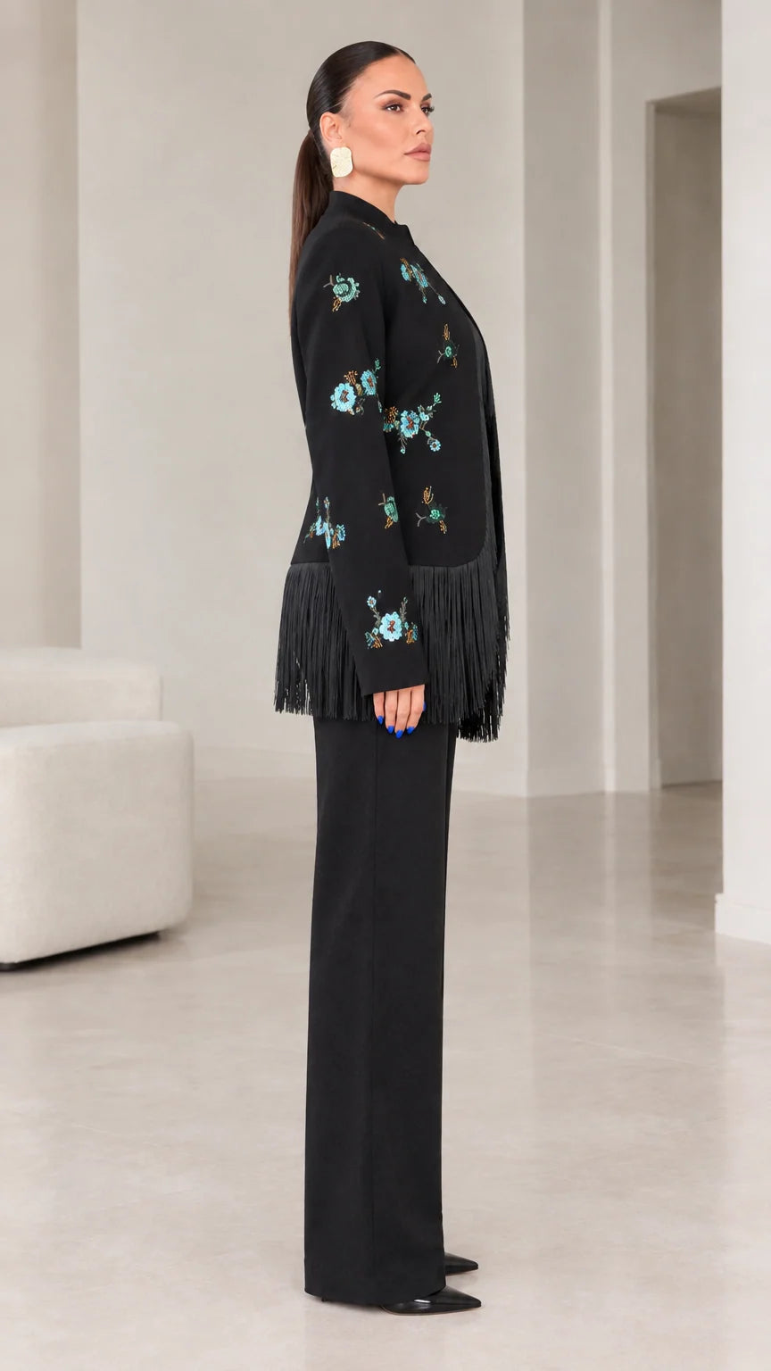 Side angle view of black embroidered blazer with fringe trim and tailored pants