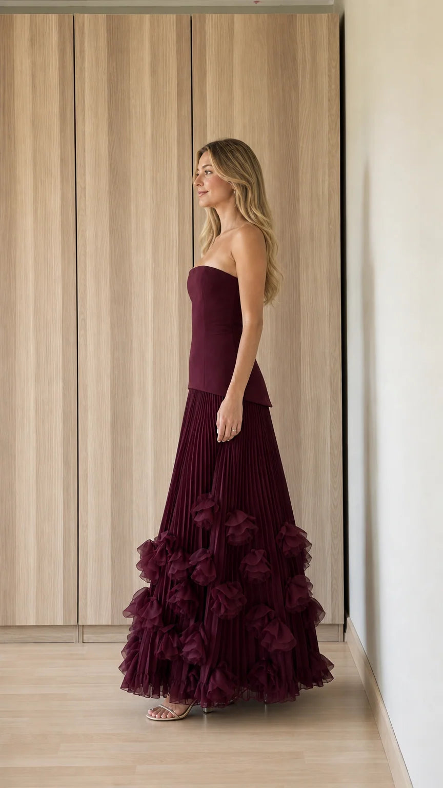 Side profile view of burgundy strapless pleated evening dress