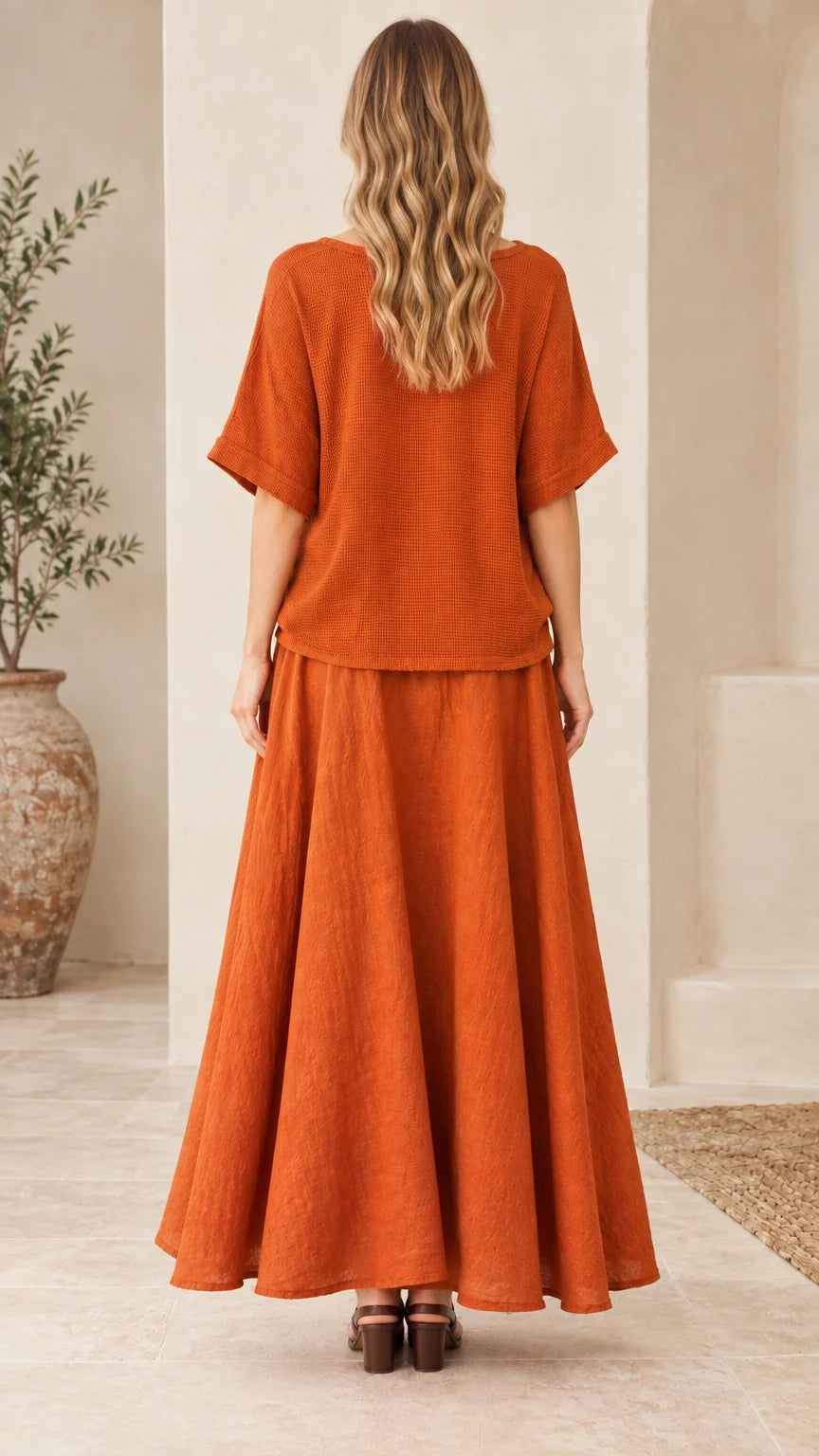 Back full-length view of woman in rust orange matching top and long skirt set