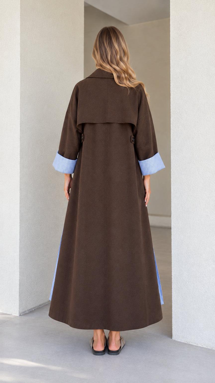 Back view of model wearing the brown maxi coat showing the classic storm flap and flowing hem
