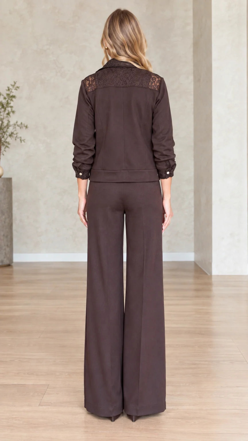 Back view of model showing lace yoke detail on dark brown jacket and straight wide trousers