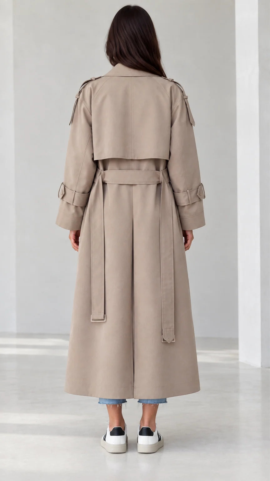 Back view of beige trench coat highlighting storm flap and belted waist design