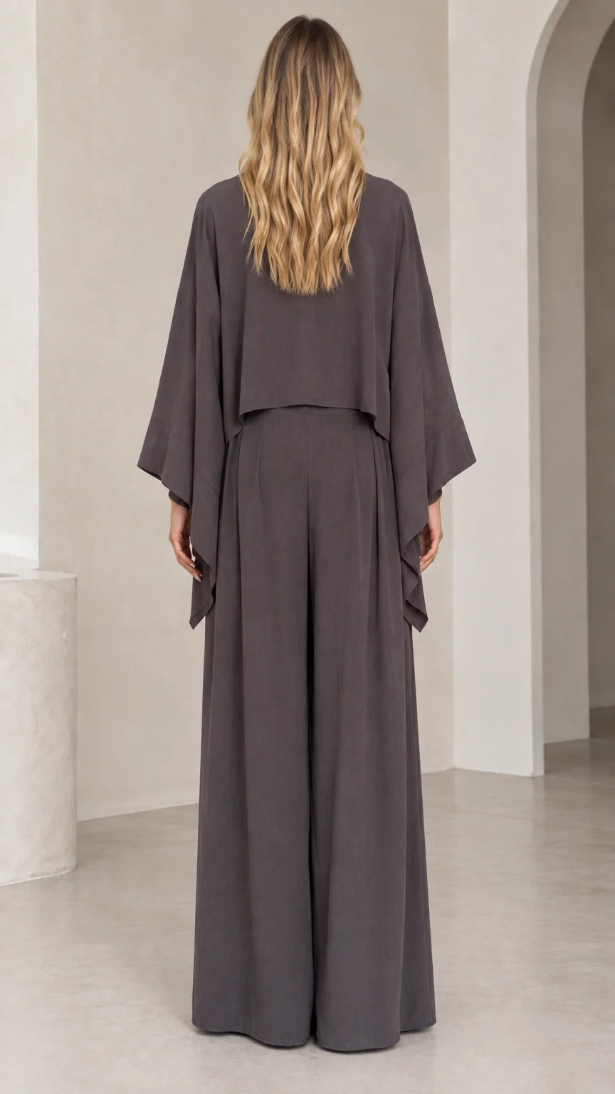 Back view of woman wearing charcoal grey draped cape sleeve top and wide leg trousers