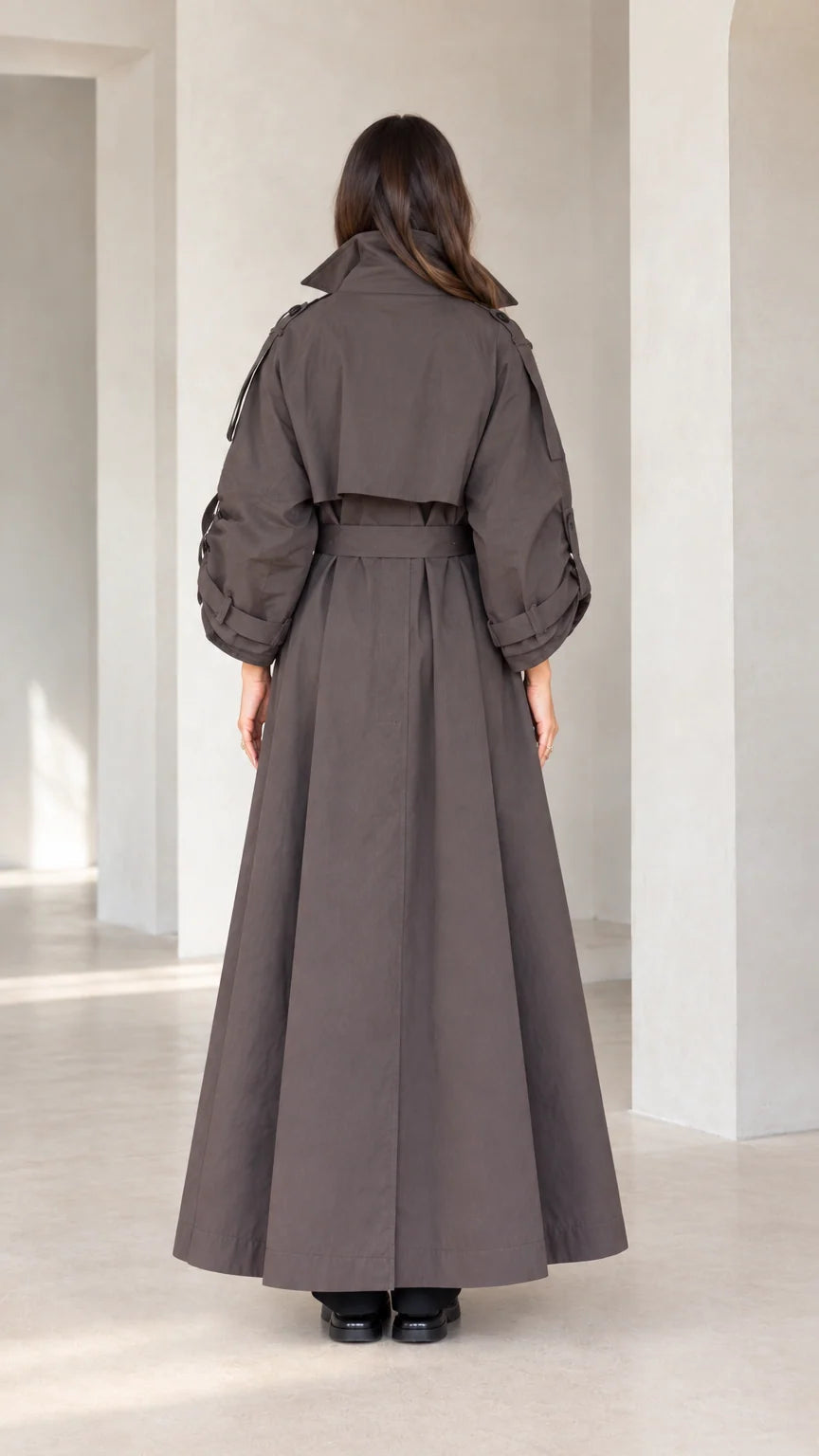 Back view of woman wearing charcoal brown belted maxi trench coat showing storm flap