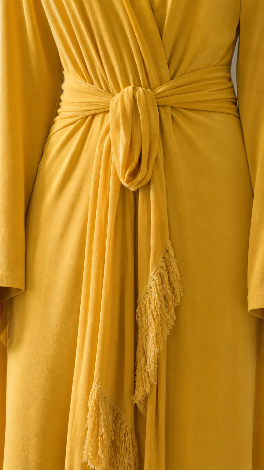 Close-up detail of the waist tie and fringe trim on yellow dress