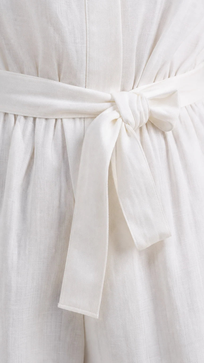 Close up view of white textured fabric and tied waist belt on jumpsuit