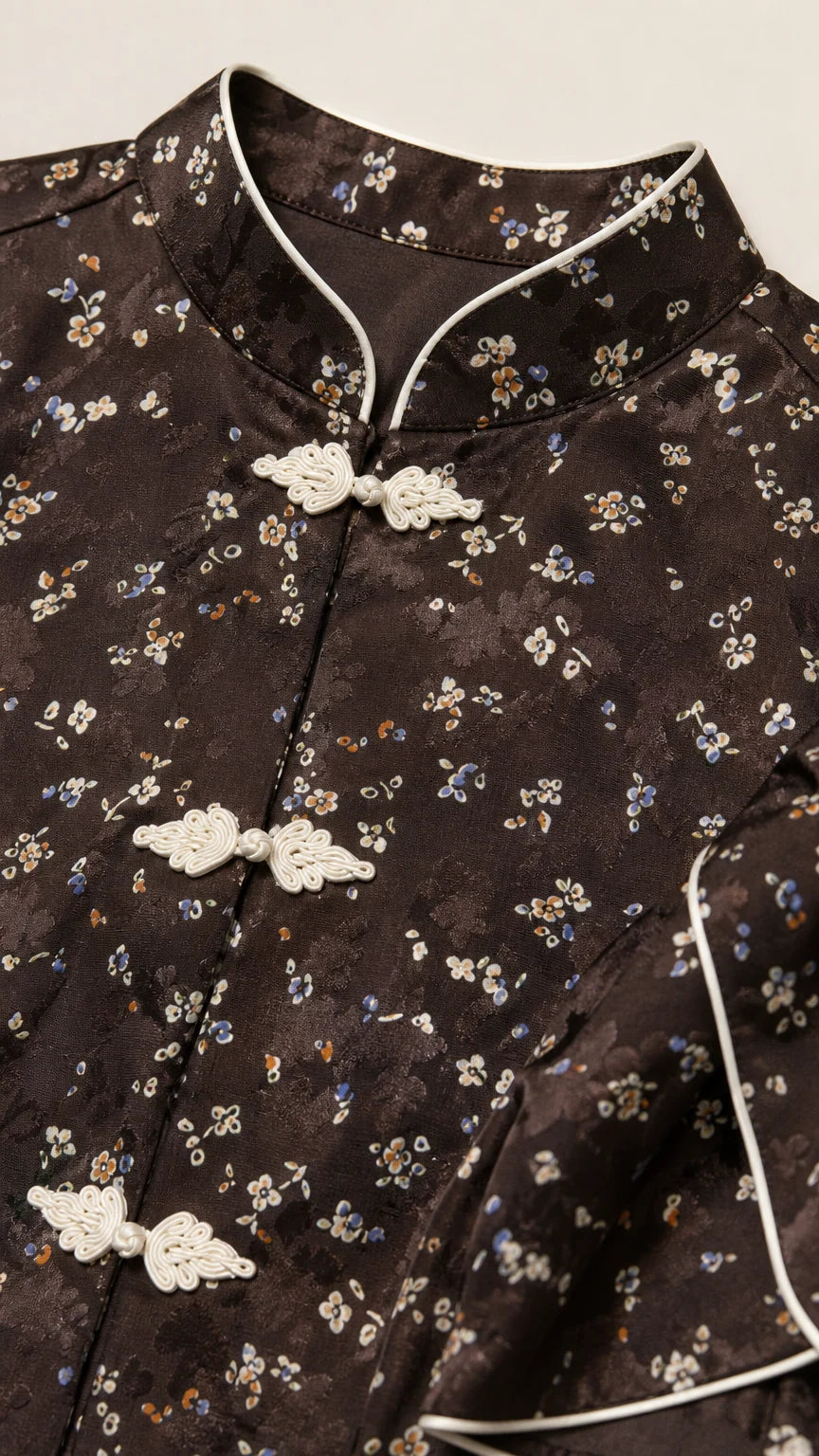 Close-up of Mandarin collar, white piping, and frog closures on dark brown floral fabric