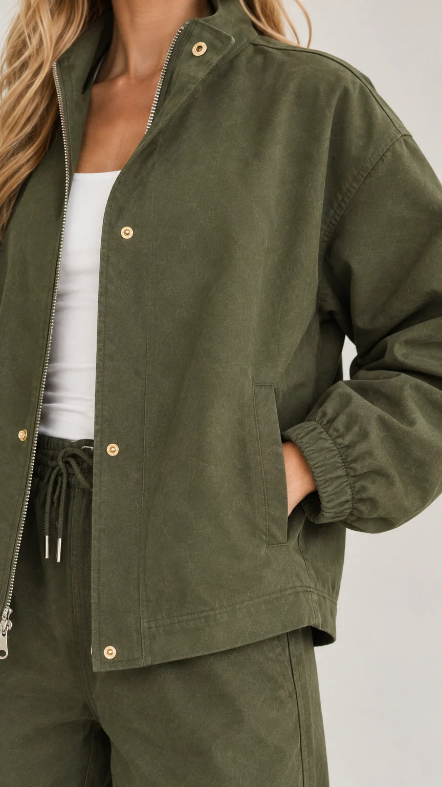 Close-up detail of olive green jacket zipper, snap buttons, and drawstring waist