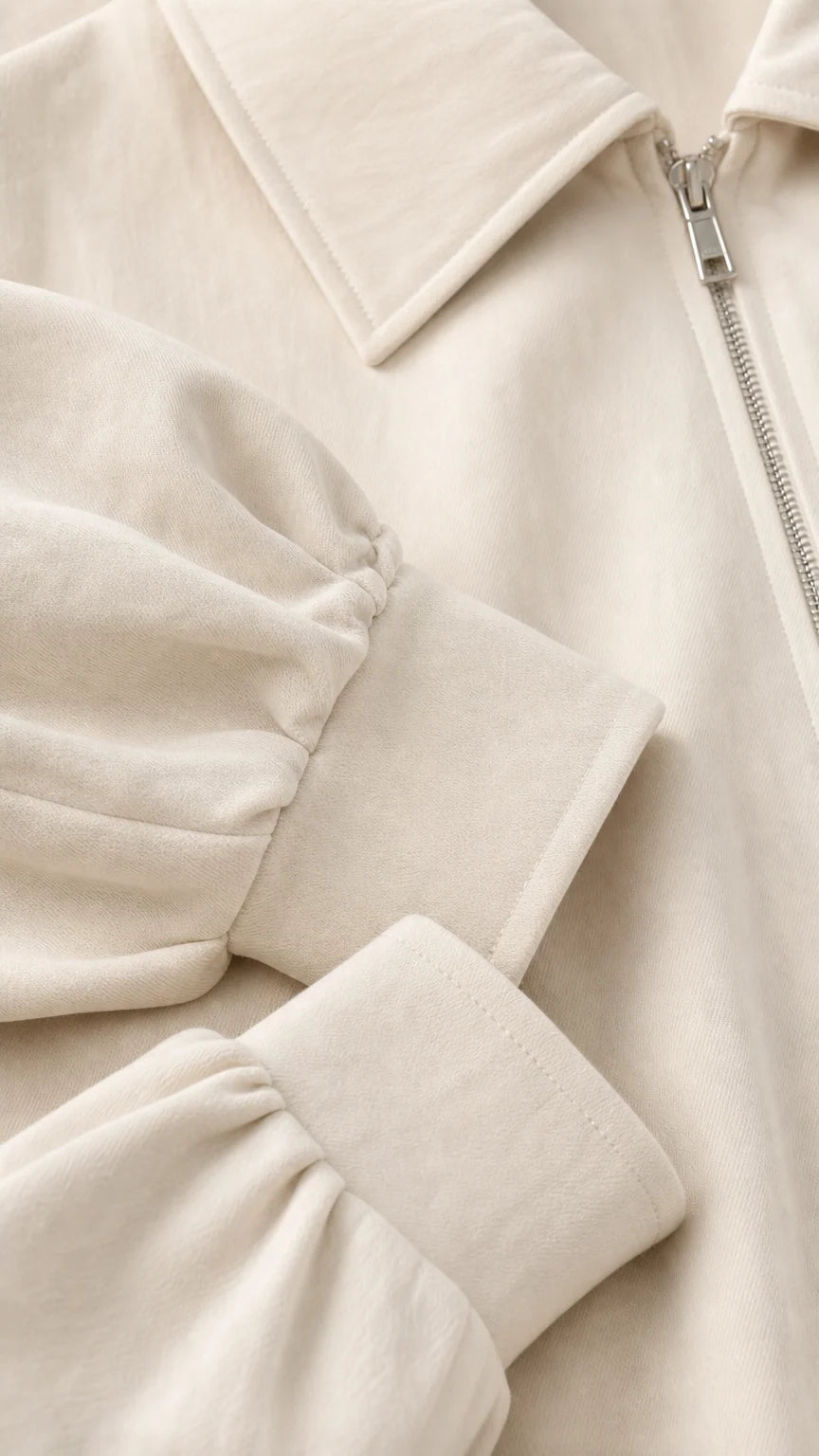 Close-up detail of cream jacket collar, metallic zipper, and gathered cuff