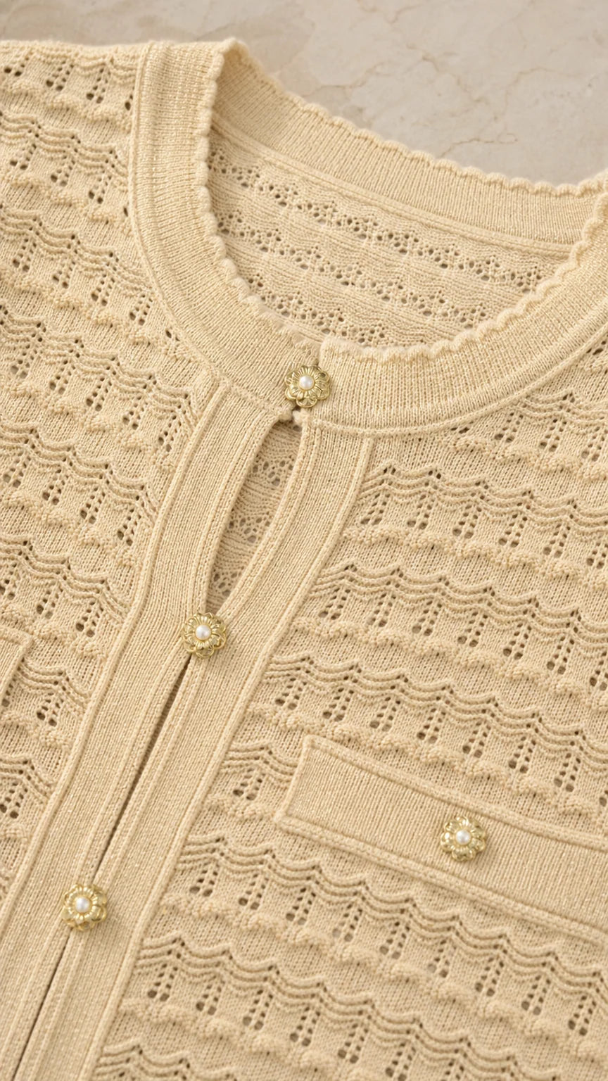 Close-up detail of beige knit top featuring pearl buttons and textured pattern