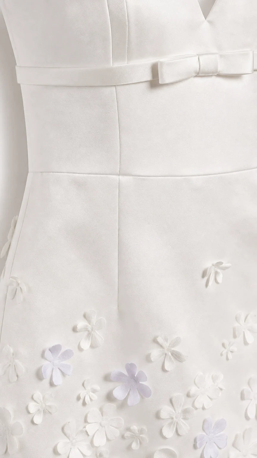 Close-up of white mini dress bodice bow and 3D floral hem