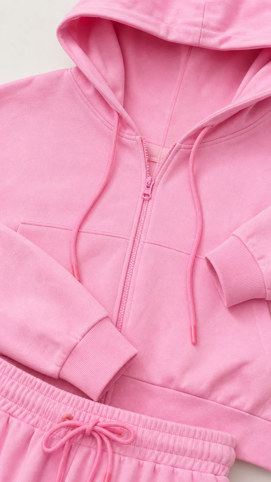 Close-up detail of pink cropped hoodie zipper, hood drawstrings, and waistband