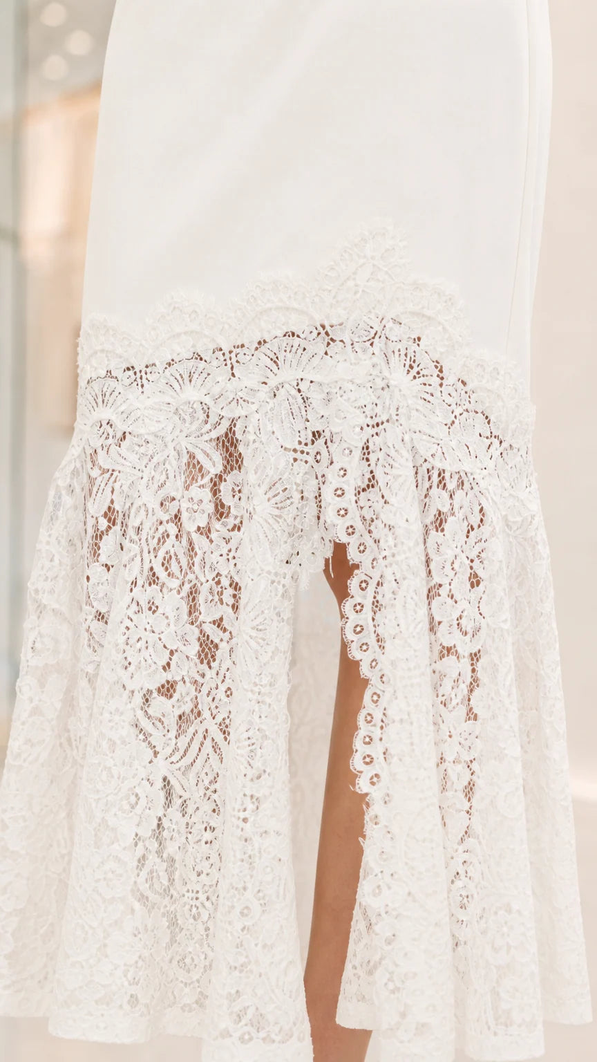 Close up view of the intricate white sheer floral lace hem with side split detail