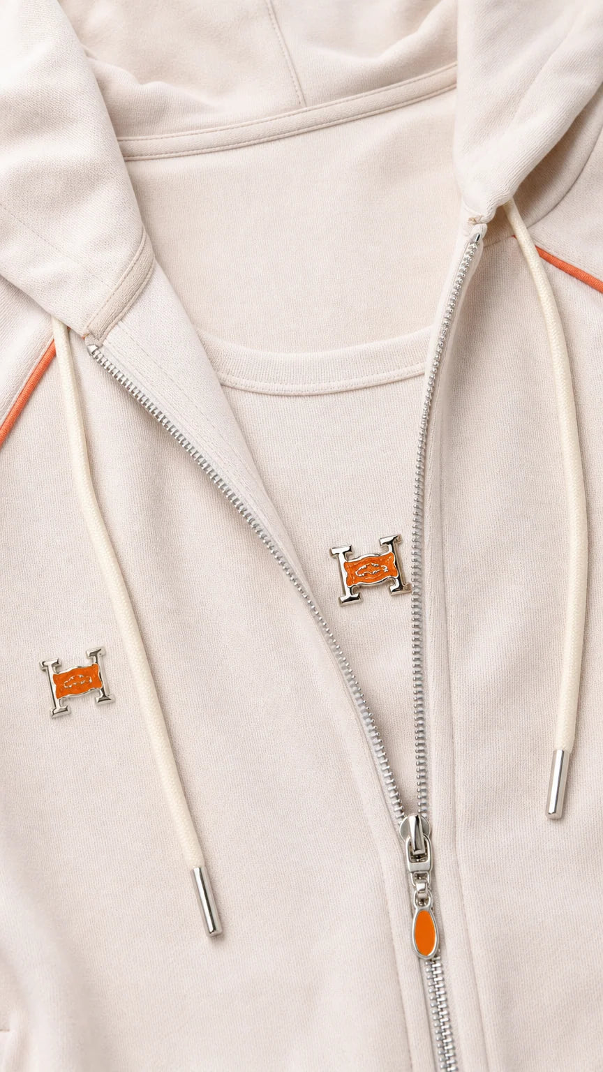 Close-up detail of beige zip hoodie with contrast orange piping and metallic zipper hardware
