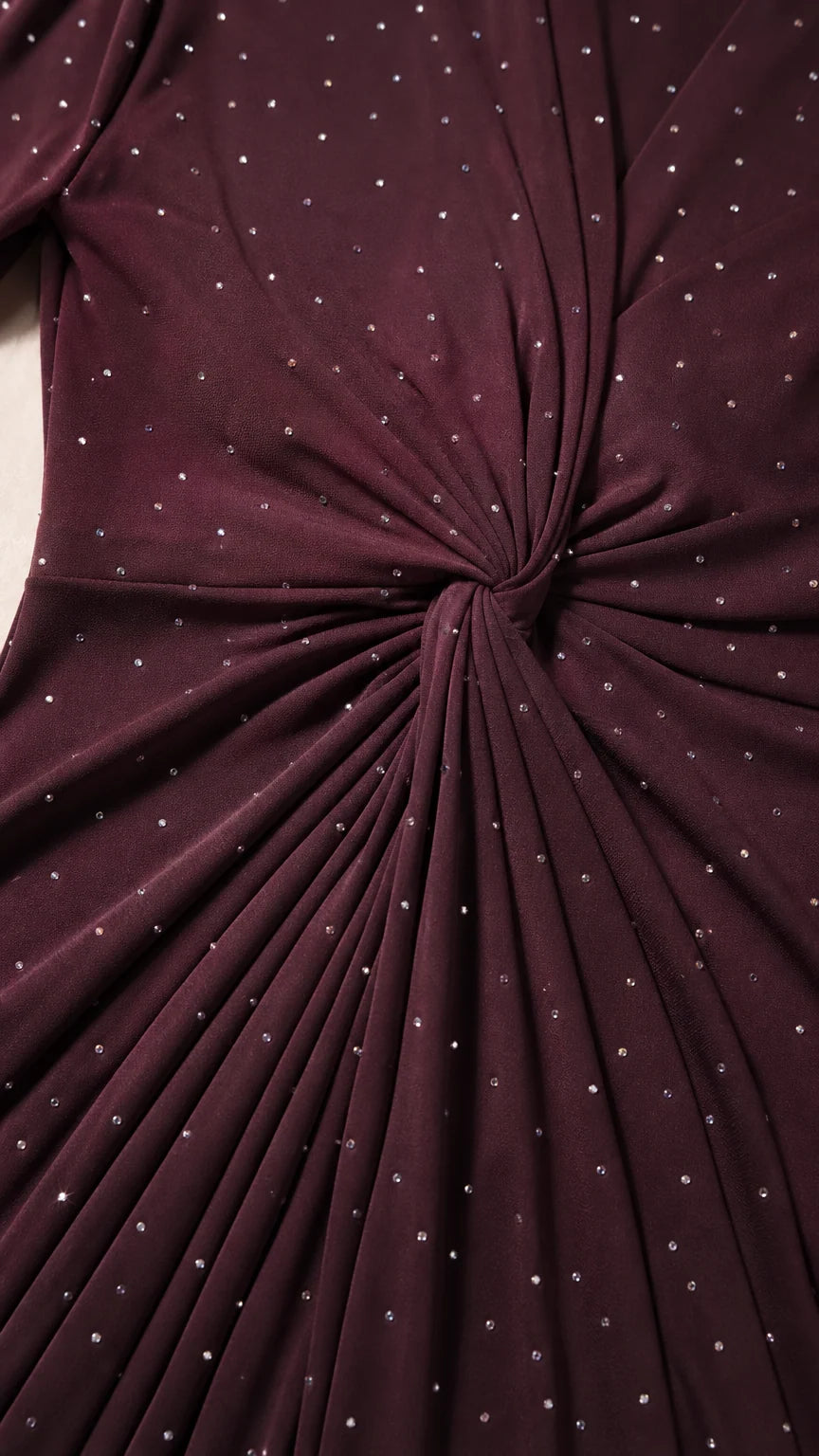 Close-up detail of twist knot waist and sparkling rhinestone embellishments on dark fabric